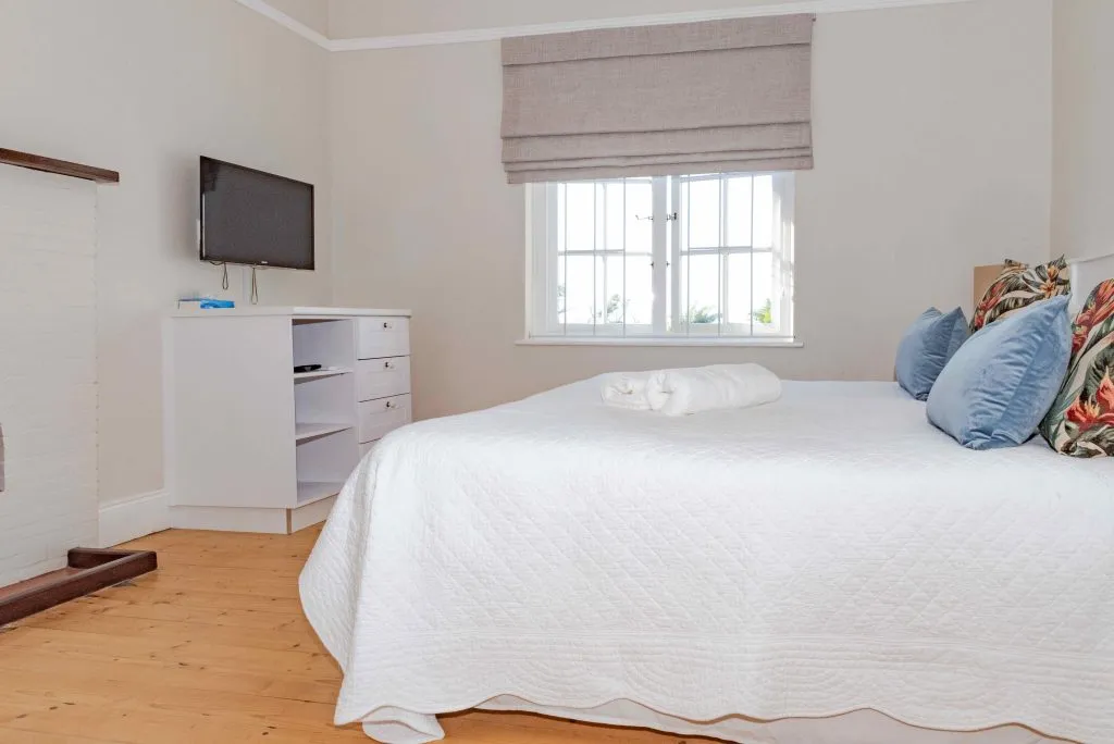 Bright bedroom with white bed wooden floor TV and window with blinds