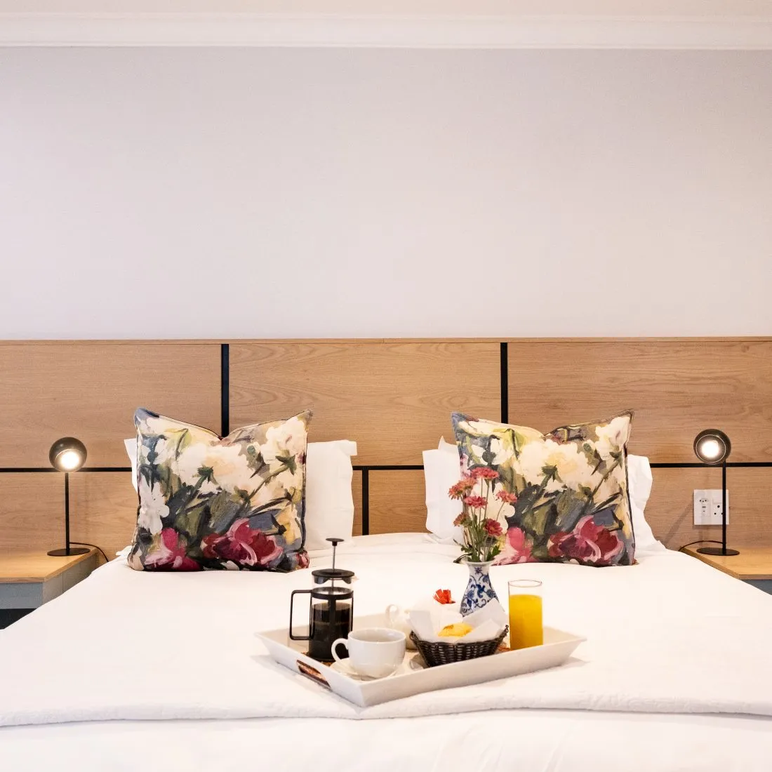 Wooden headboard with pillows breakfast tray on bed bedside lamps and flowers