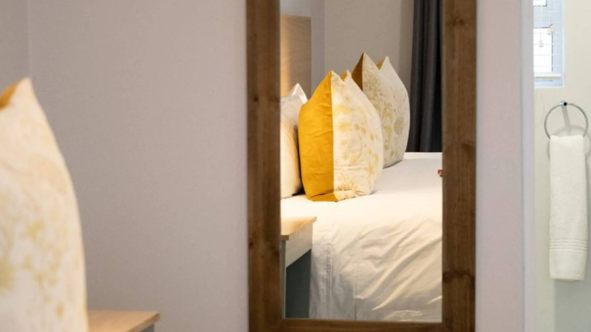 Reflection of a bed with yellow and white pillows in a woodenframed mirror