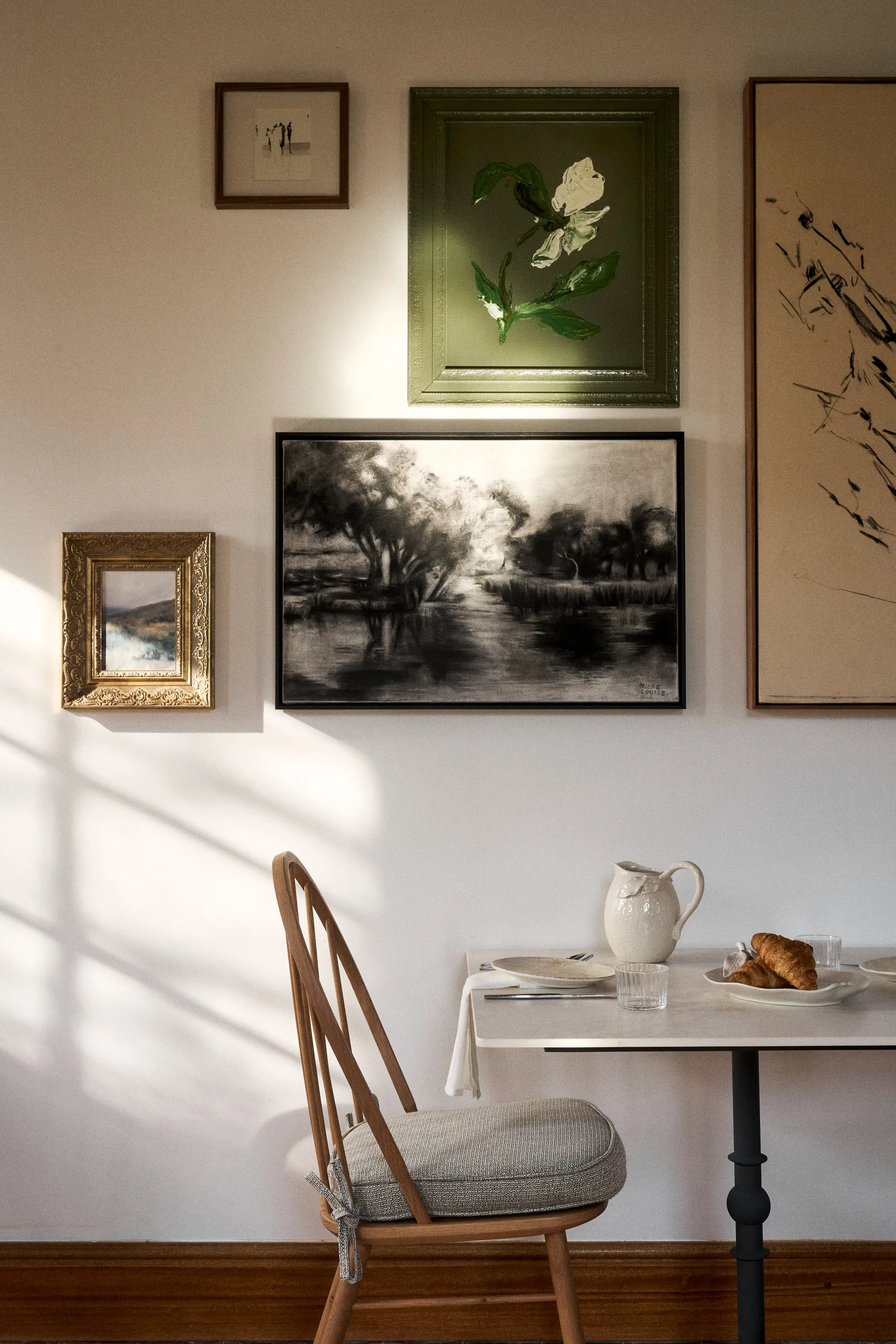 Wooden chair and table with pitcher and croissant under framed wall art