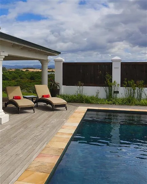 Two lounge chairs by a pool with a wooden deck and white columns