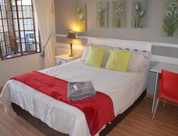 Bedroom with white bed red throw green pillows and wooden floor