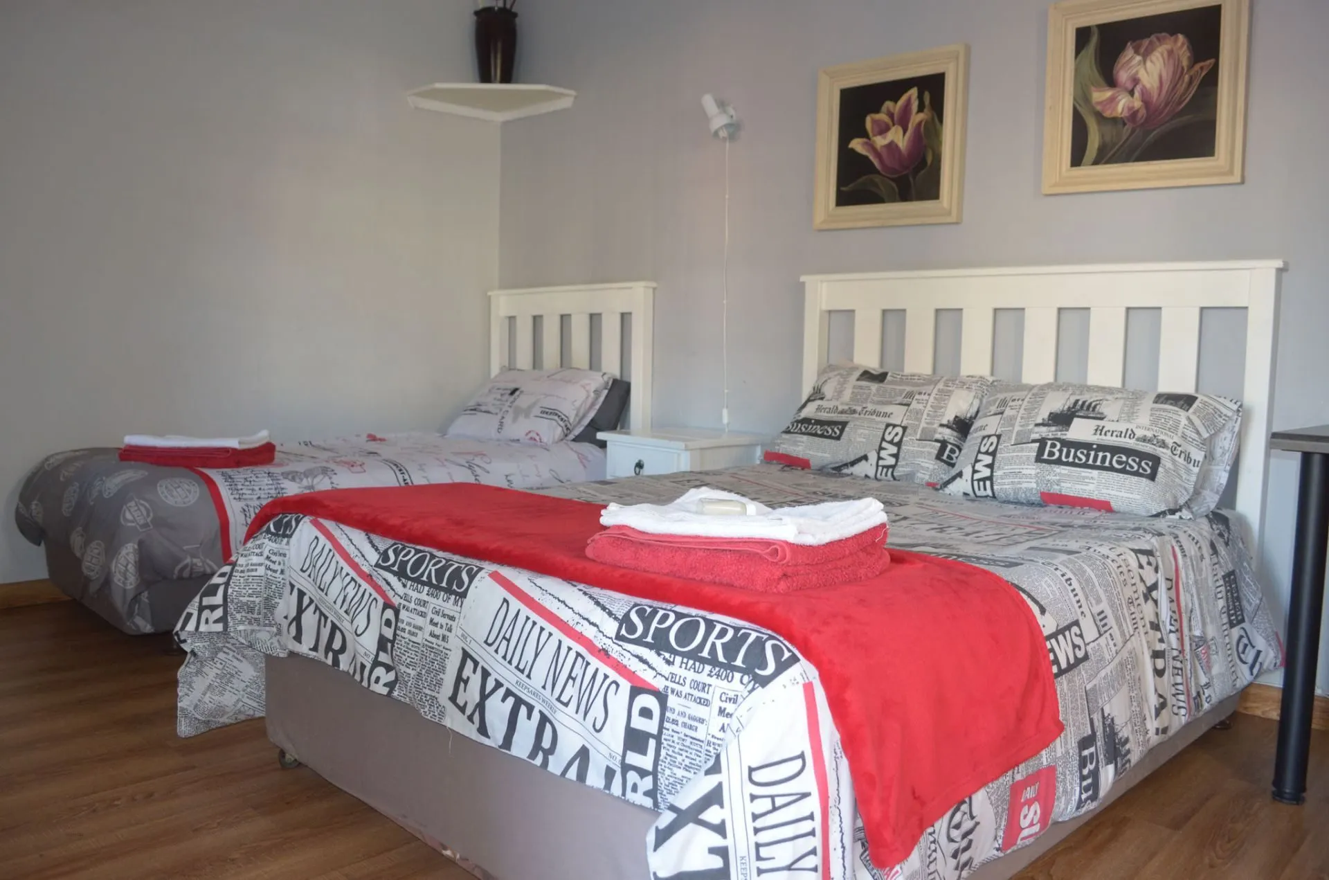 Two beds with newspaper print bedding in a bedroom with floral wall art