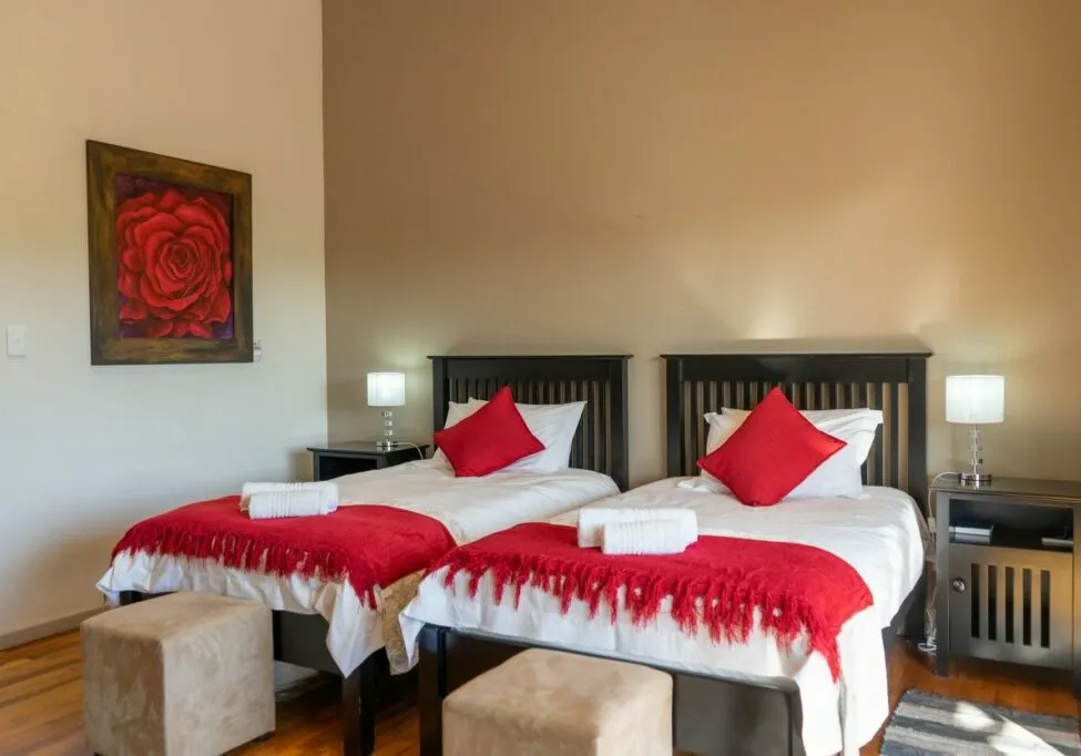 Two single beds with red blankets and pillows in a bedroom with wooden floor