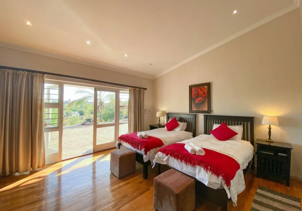 Bright bedroom with two beds red blankets and large windows with curtains