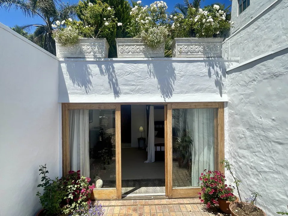 White courtyard with potted plants and flowers in front of a wooden door