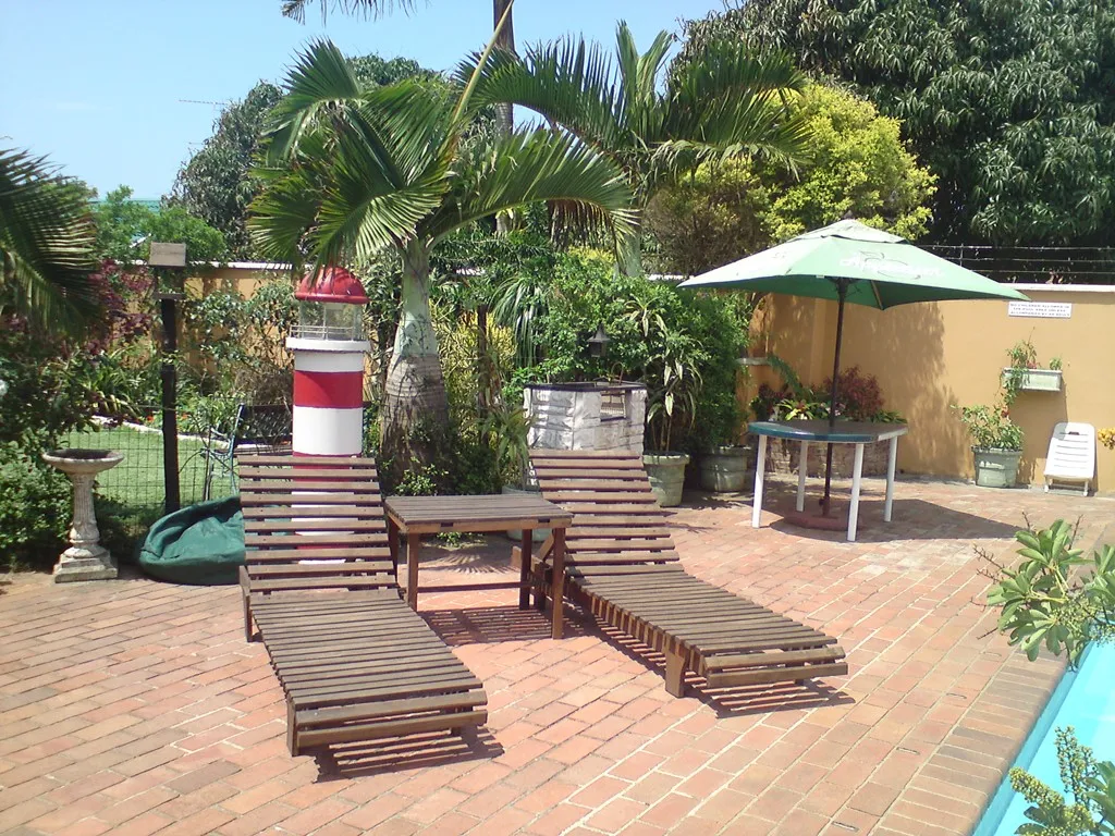 Wooden lounge chairs on a brick patio with a pool and garden