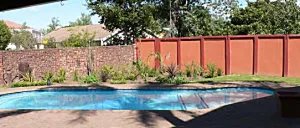 Swimming pool in a backyard with a brick wall and plants