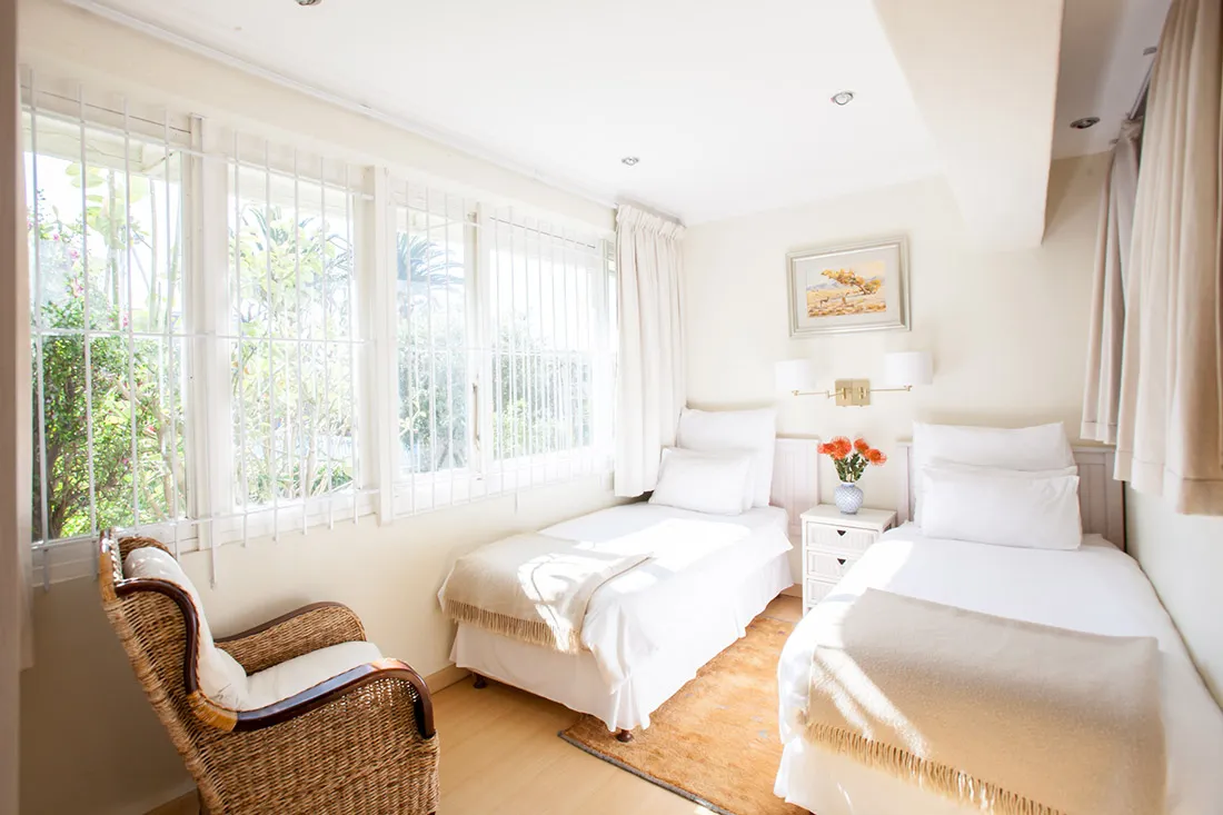 Bright bedroom with two single beds wicker chair and large windows