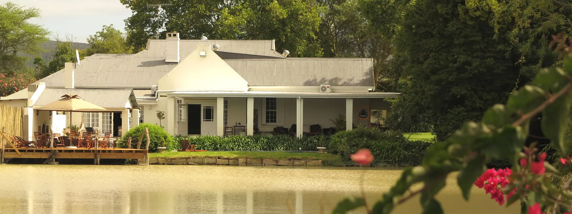 House by a lake with trees and flowers in the foreground