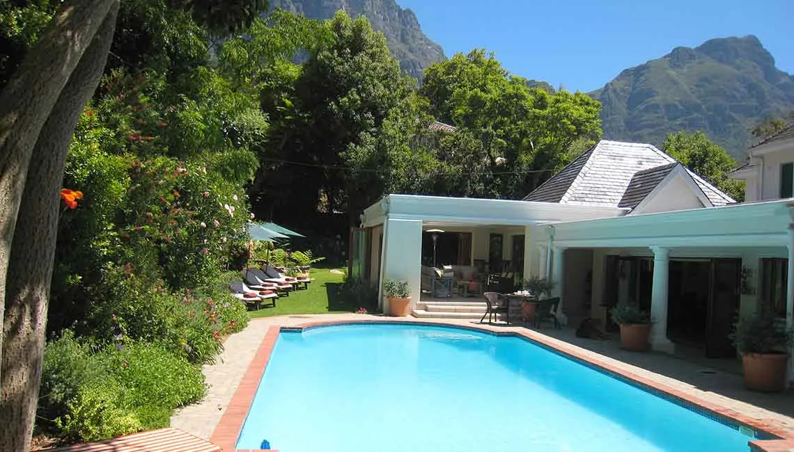 Swimming pool with lounge chairs surrounded by greenery and mountains in the background