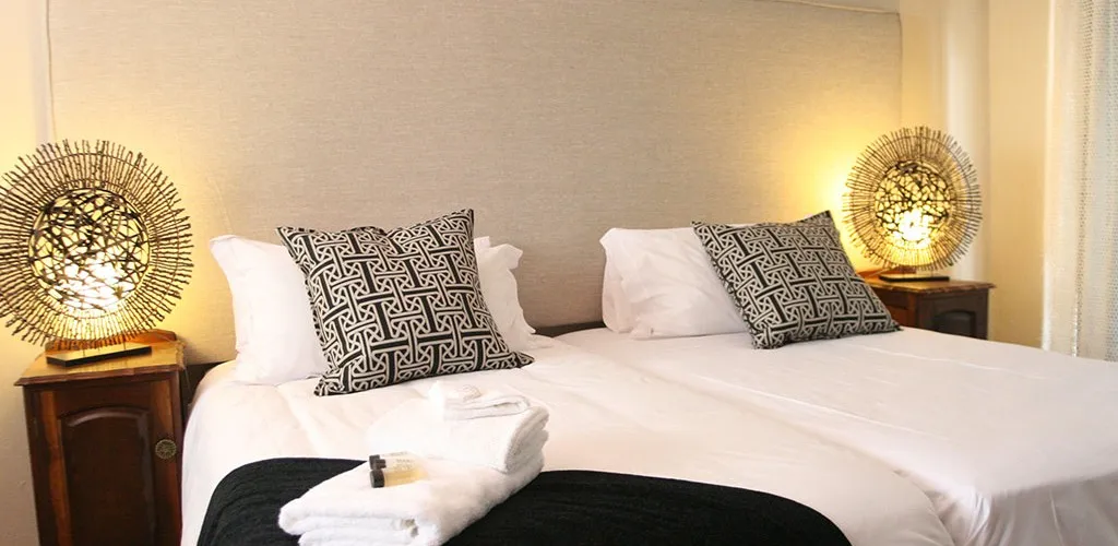 Two beds with patterned pillows white towels and bedside lamps in a bedroom