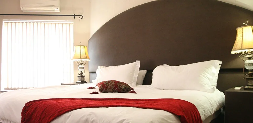 Large bed with white linens and red throw flanked by two bedside lamps