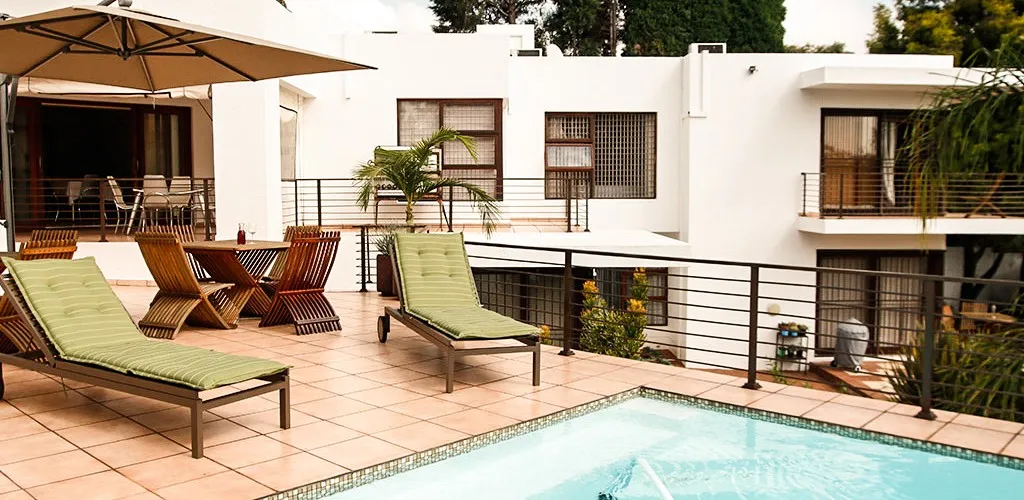 Outdoor patio with lounge chairs dining table and pool near modern white buildings