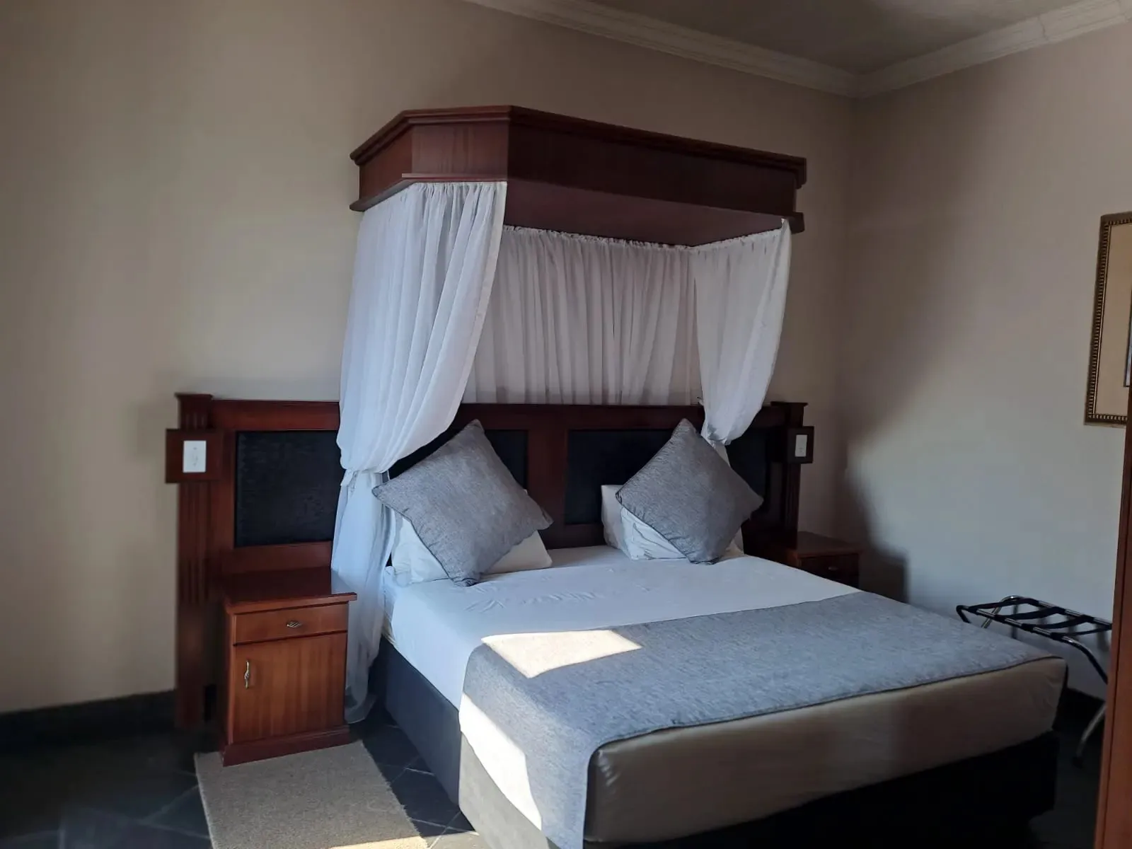Large bed with wooden headboard and white canopy in a bedroom