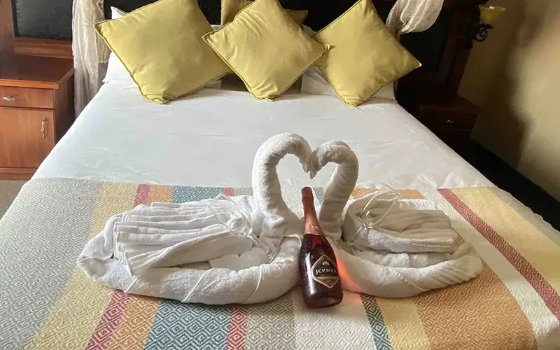 Towel swans on a bed with a bottle of wine between them