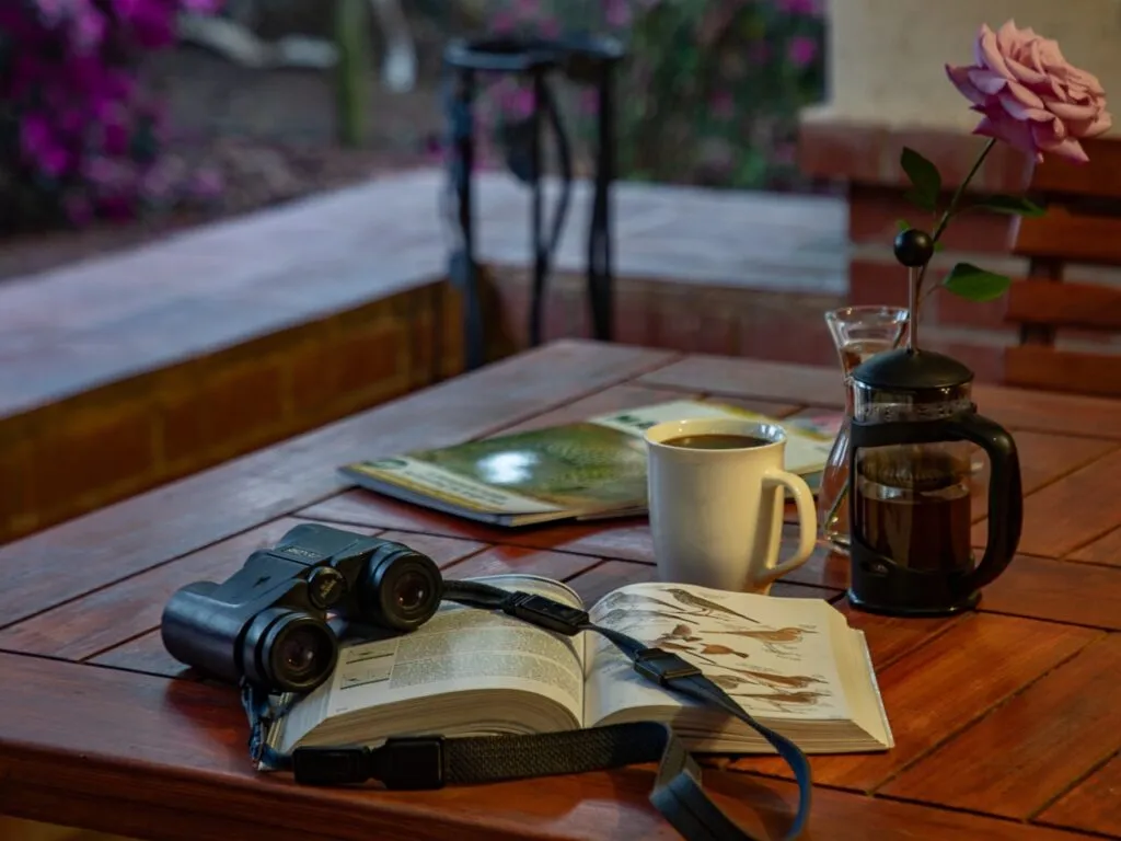 Open book binoculars coffee cup and flower on a wooden table outdoors