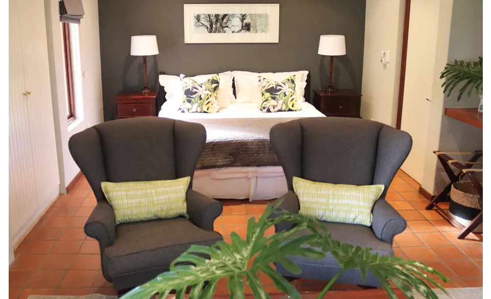 Two armchairs in a bedroom with a bed and nightstands in the background