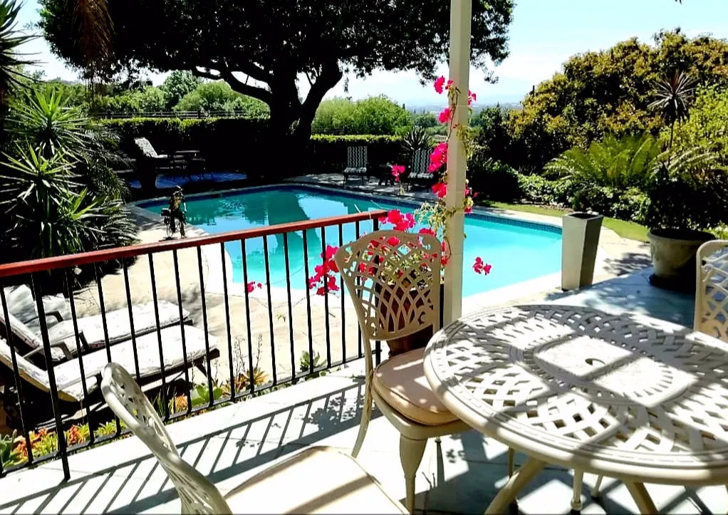 Patio with table and chairs overlooking a swimming pool and garden