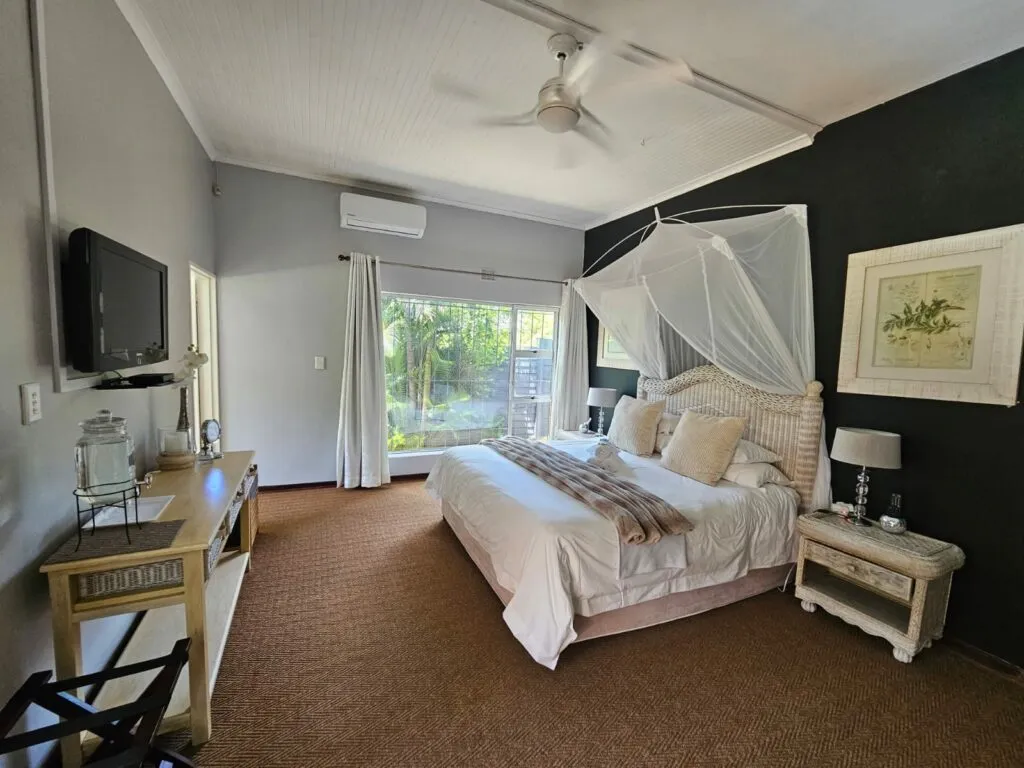 Bedroom with large bed mosquito net TV and window view of greenery
