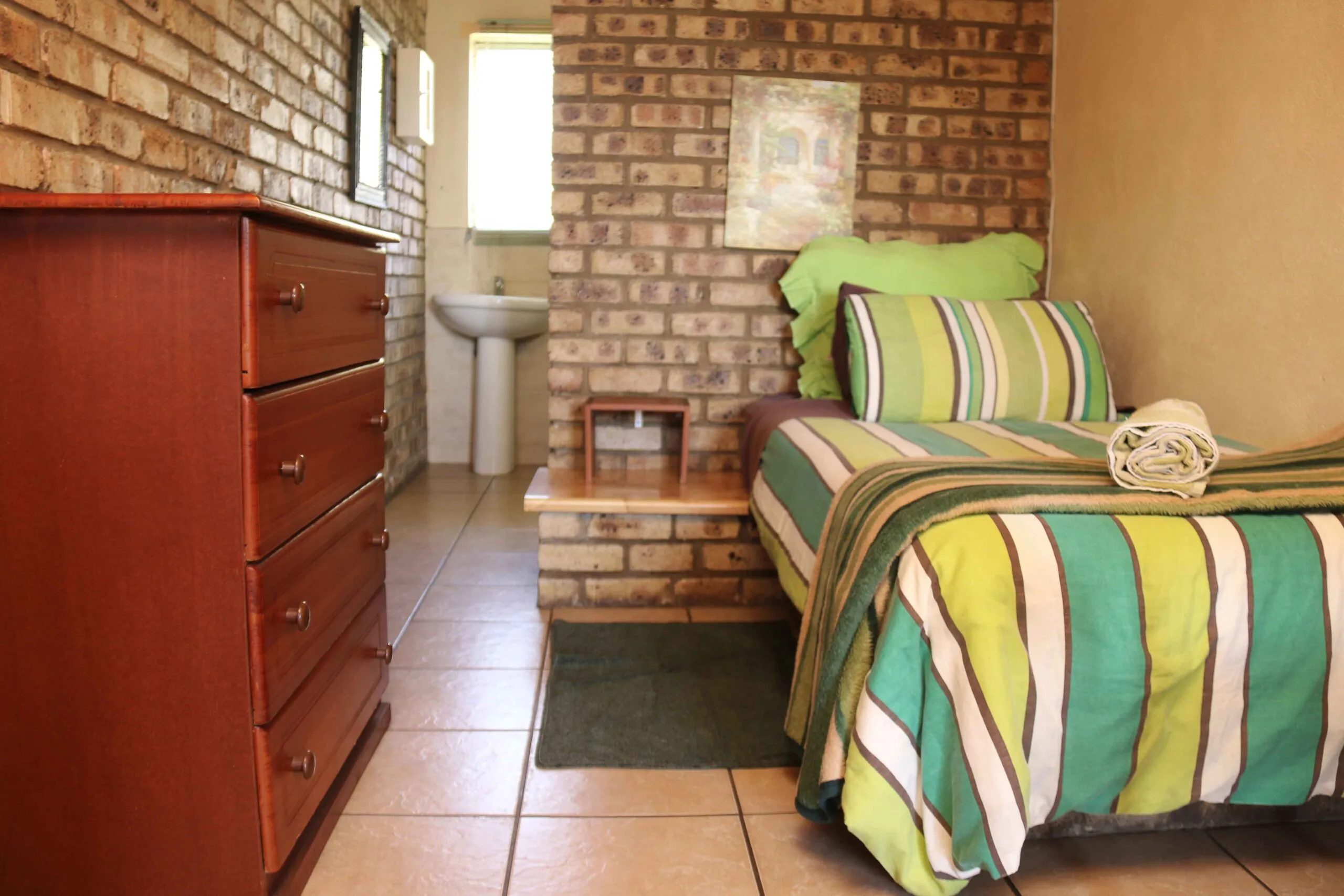 Small bedroom with a single bed wooden dresser and brick wall