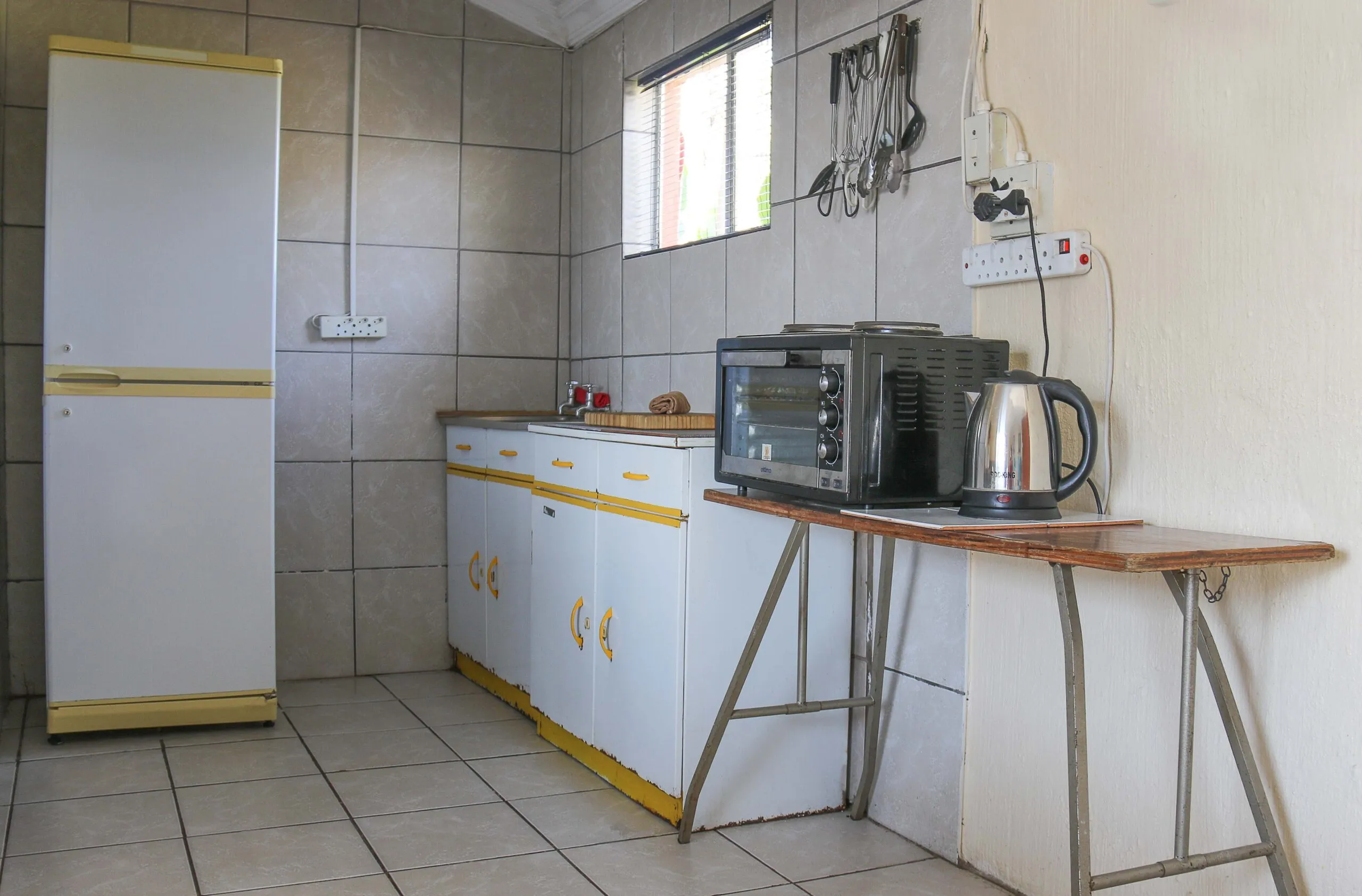 Small kitchen with white fridge microwave kettle and tiled walls and floor