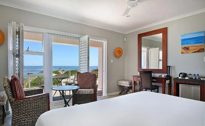 Hotel room with ocean view bed chairs desk and artwork on walls