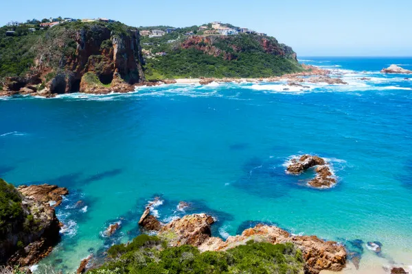 Rocky coastline with clear blue water and green vegetation under a sunny sky