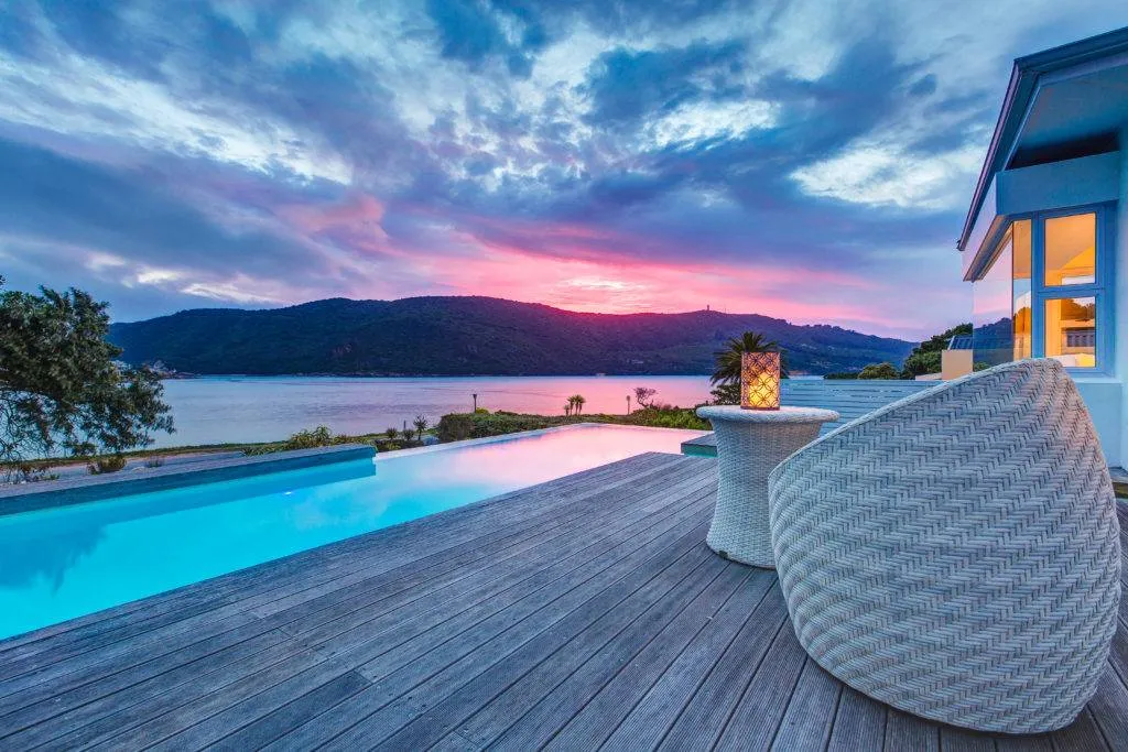 Modern deck with pool wicker furniture and scenic sunset over mountains and water