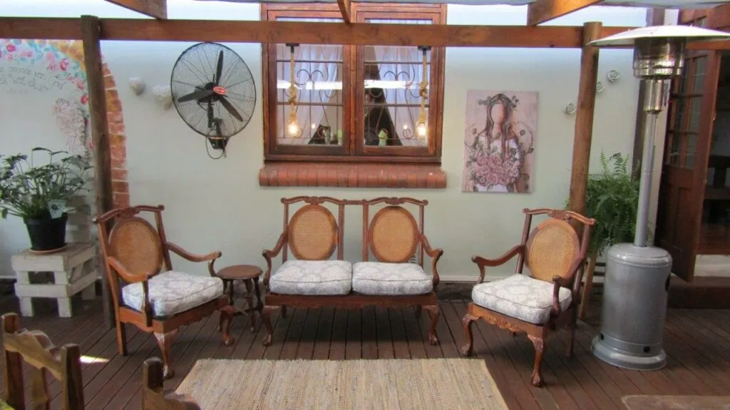 Wooden chairs and sofa on a wooden deck with plants and a wall fan