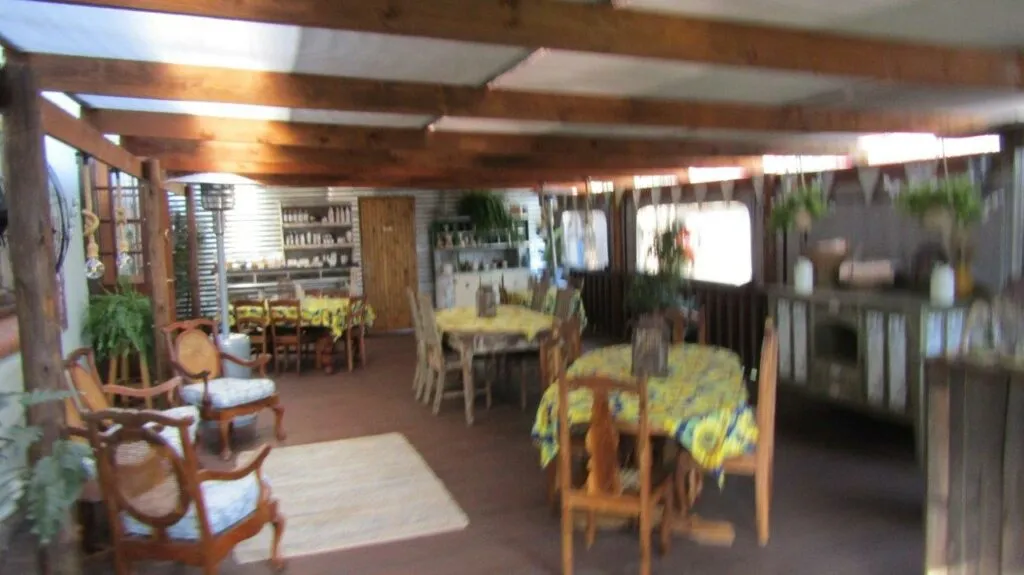 Wooden patio with tables chairs and plants covered by a wooden roof