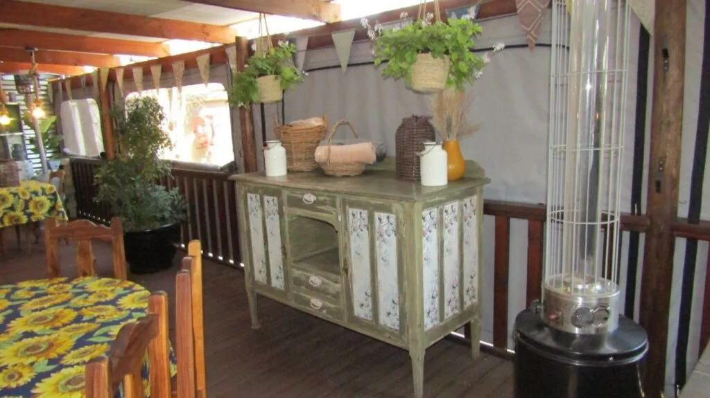 Wooden sideboard with decor in outdoor dining area with yellow and blue tablecloths