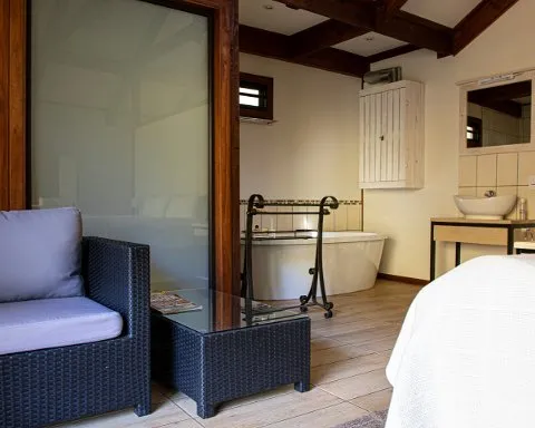Cozy bedroom with attached bathroom featuring a bathtub sink and wicker furniture
