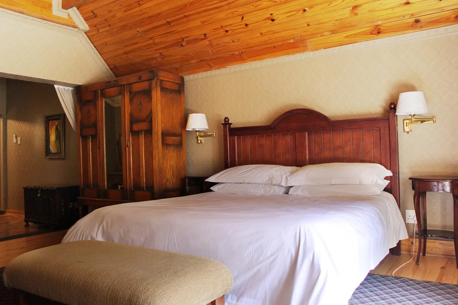 Wooden bedroom with large bed wooden headboard and matching furniture under slanted ceiling
