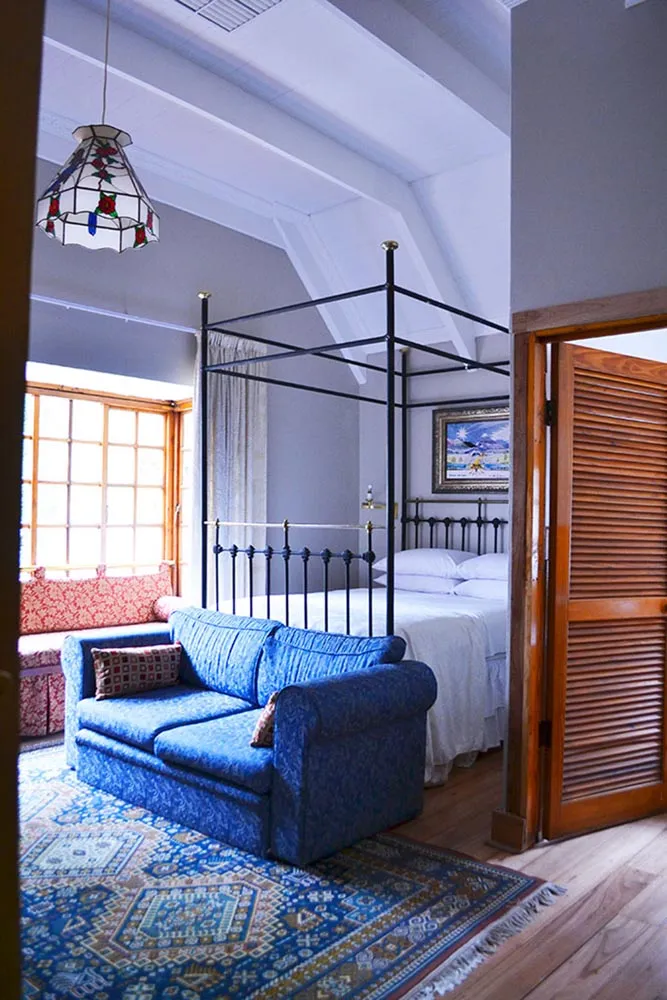 Cozy bedroom with blue sofa iron bed wooden shutters and patterned rug