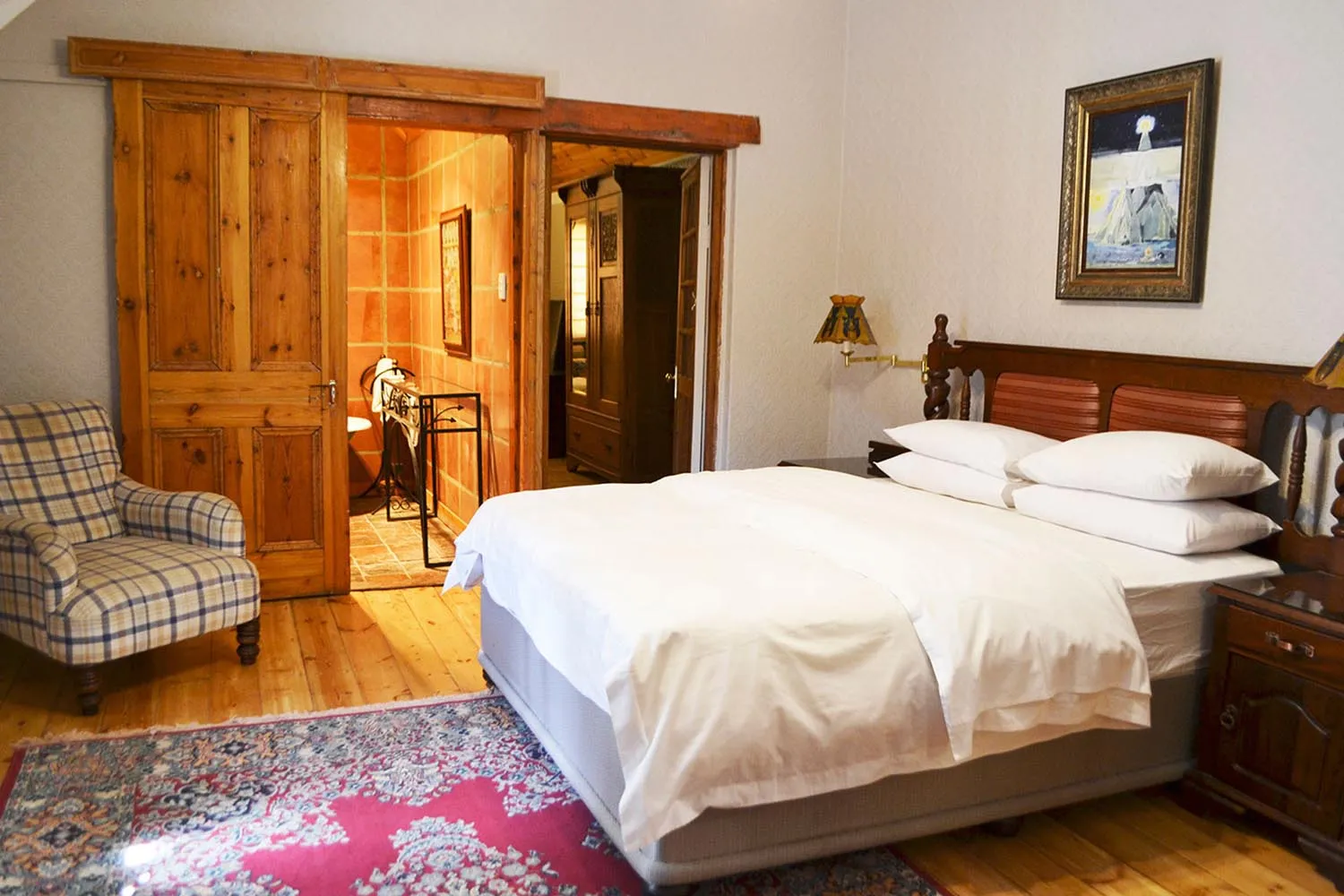 Wooden bedroom with large bed plaid chair and sliding door to bathroom