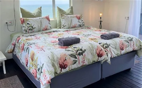 A floral bed with pillows and towels in a bright room with ocean view