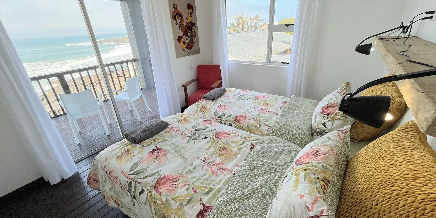 Bedroom with floral bedding ocean view and balcony with chairs