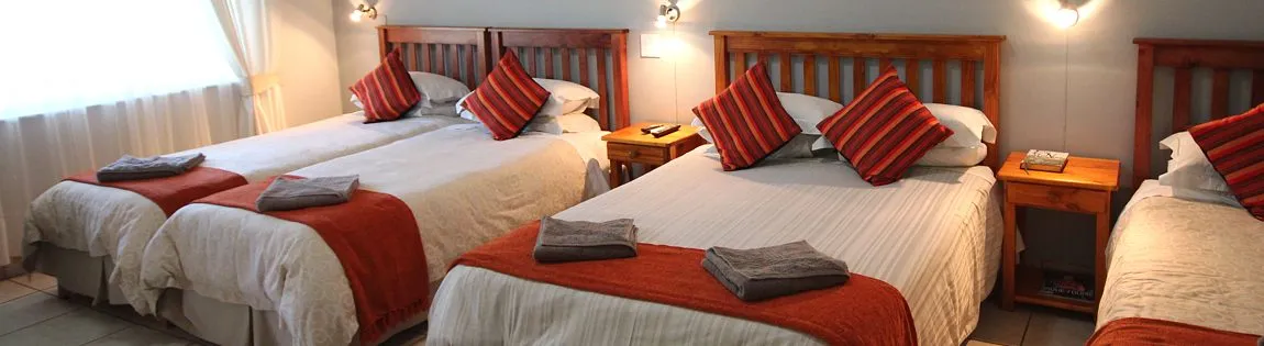 Three neatly made beds with red and grey pillows in a bright room