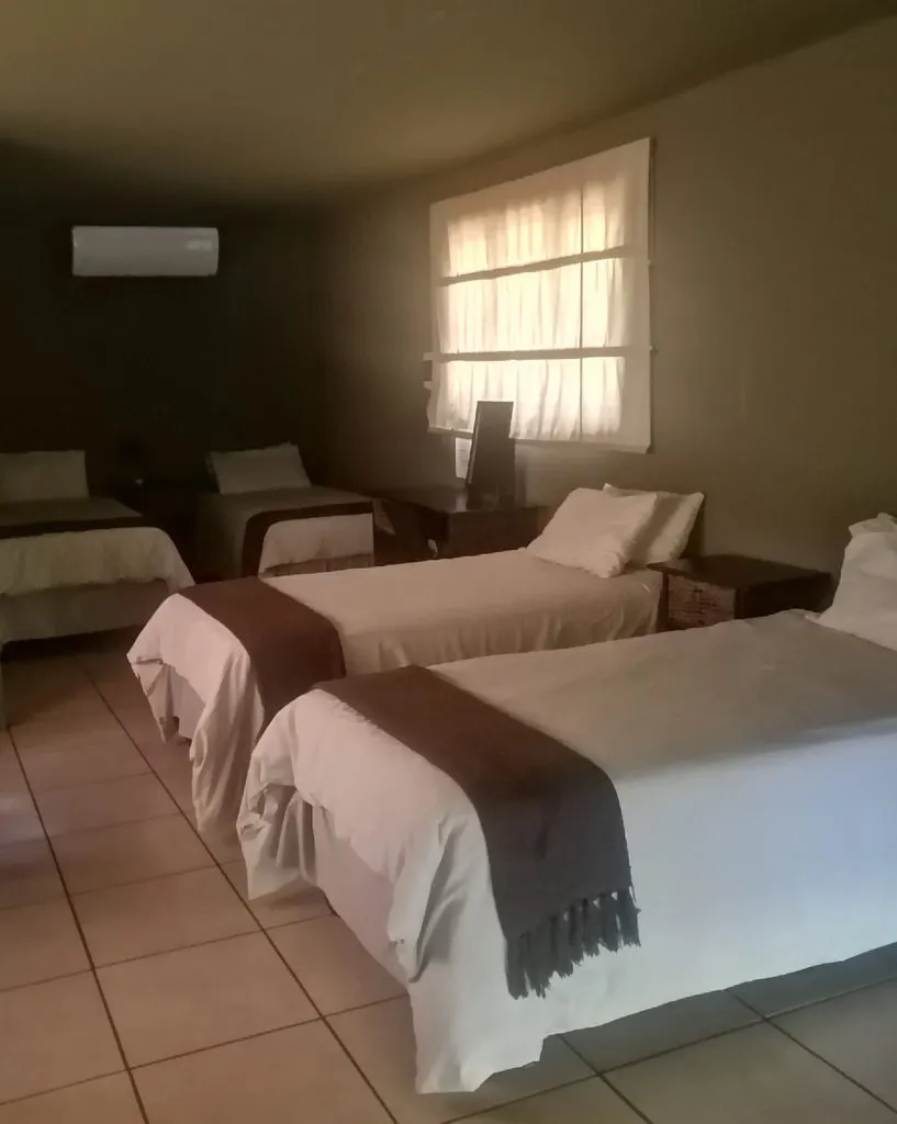Three beds in a dimly lit room with a window and air conditioner