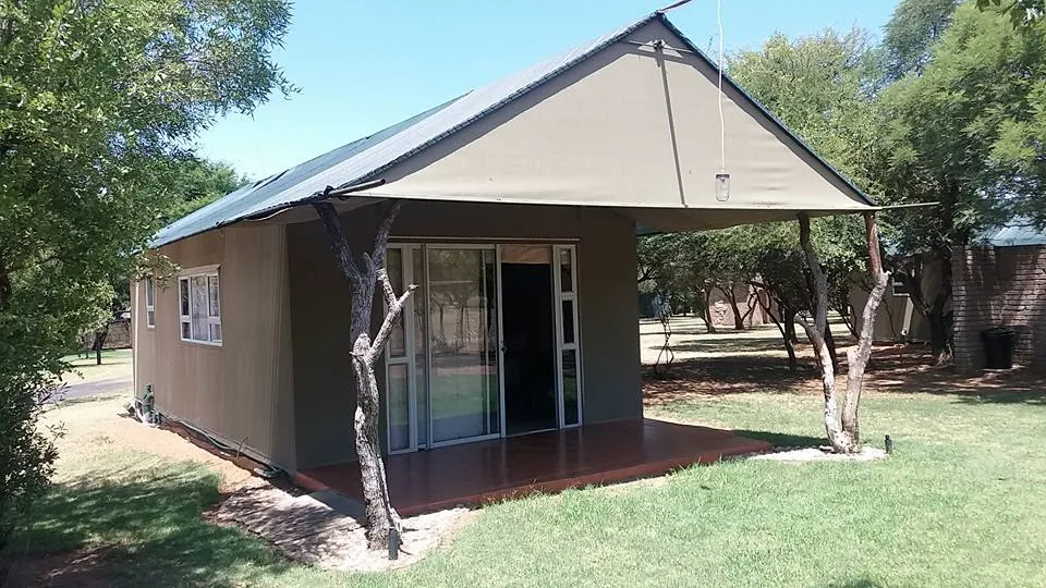 Small brown cabin with a covered porch in a grassy treelined area