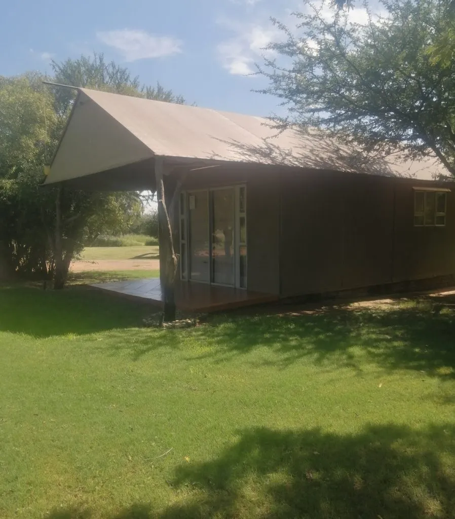 A wooden cabin with a veranda in a grassy area under trees