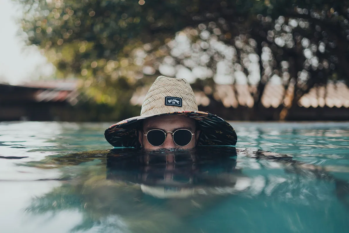 Person in a straw hat and sunglasses partially submerged in a pool