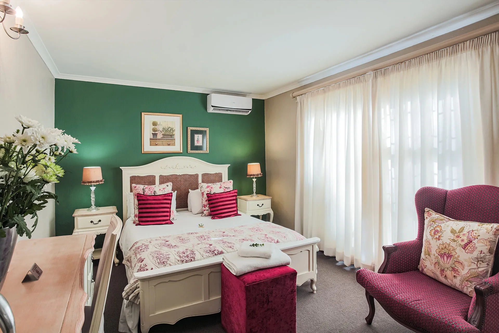 Cozy bedroom with green accent wall white bed and floral armchair by window