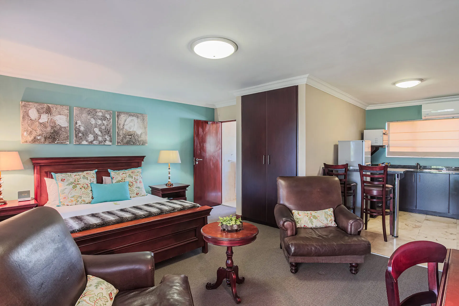 Cozy bedroom with a bed armchairs and a small kitchenette