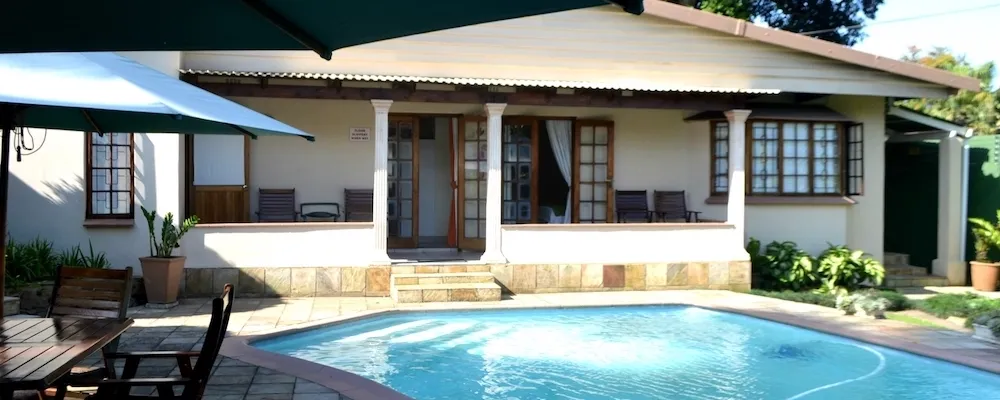 House with a patio pool and outdoor seating area under umbrellas