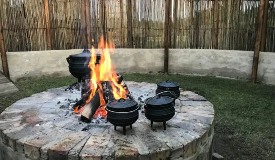 Three black pots over a fire pit in a garden with a bamboo fence