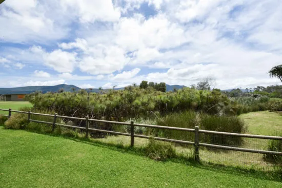 Grassy field with wooden fence and bushes under a partly cloudy sky