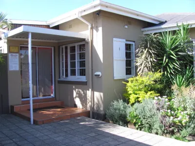 Beige house with red steps plants in front and a clear blue sky
