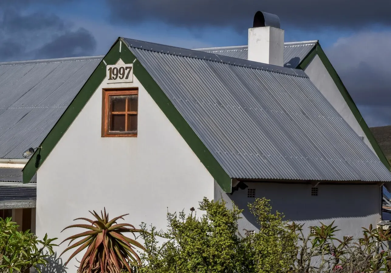 White house with green trim corrugated metal roof and a small window